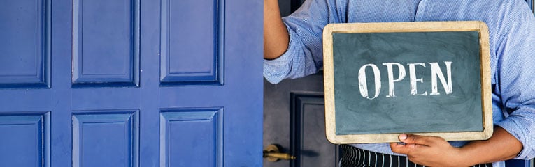 Man-in-blue-shirt-holding-blue-door-with-open-sign-after-learning-how-to-start-a-business.
